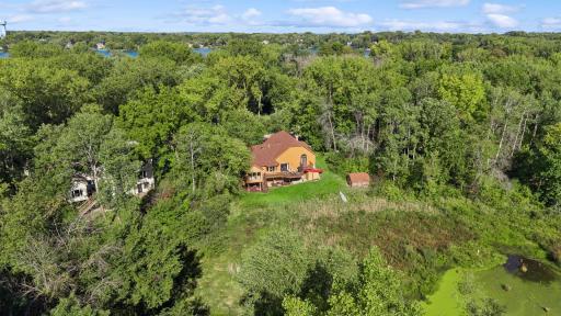 Aerial view highlights the home’s wooded setting, backyard pond and wetlands, mature trees, and privacy, with Lake Gervais nearby.
