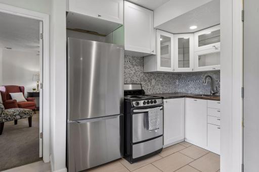 Lower-level kitchen features white cabinetry, stainless steel appliances, tile backsplash, and plenty of storage.
