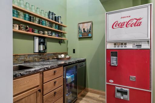 Convenient main-level wet bar with sink, beverage refrigerator, cabinetry, open shelving, and built-in coffee maker - perfect for morning coffee or entertaining guests.