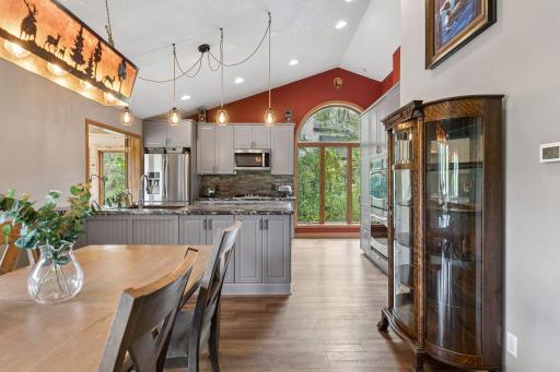 Bright kitchen features a large center island, stainless steel appliances, double oven, abundant cabinetry, and a dramatic arched window overlooking the wooded setting.