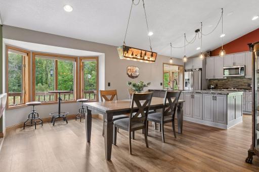 Dining area with large windows and beautiful natural light opens directly to the kitchen, creating a comfortable gathering space with views of the surrounding trees.