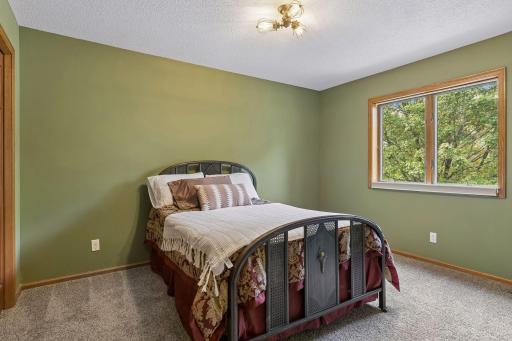 Comfortable upper-level bedroom with a large window bringing in natural light and views of the mature trees.
