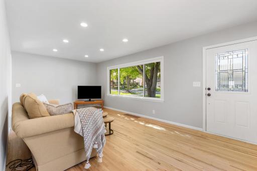 Sun-drenched living room showcasing gleaming natural hardwood floors, crisp neutral paint, and oversized picture windows.
