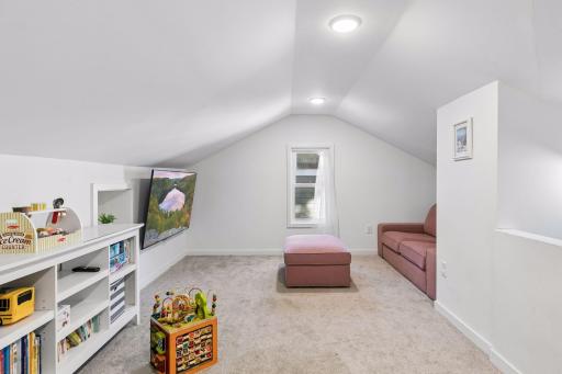 Spacious upper-level third bedroom with vaulted ceilings, recessed lighting, and flexible space for a sitting or play area.