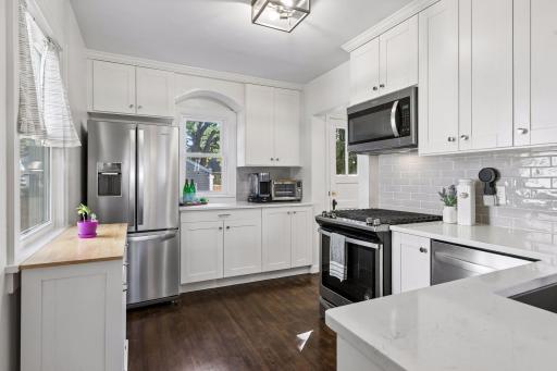 Updated kitchen with white soft-close cabinetry, stainless-steel appliances, tile backsplash, generous counter space, and hardwood floors.