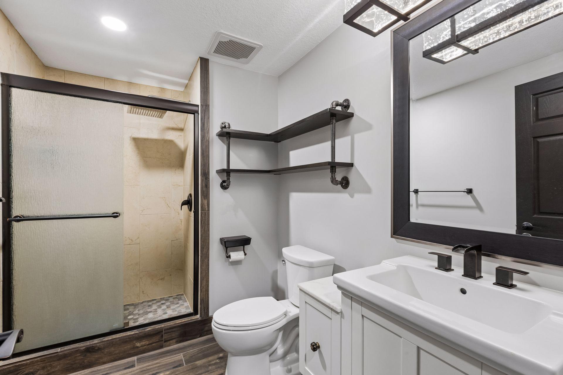 The remodeled three-quarter bathroom in the lower level features a tiled shower with rain-glass doors, modern fixtures, and convenient open shelving.