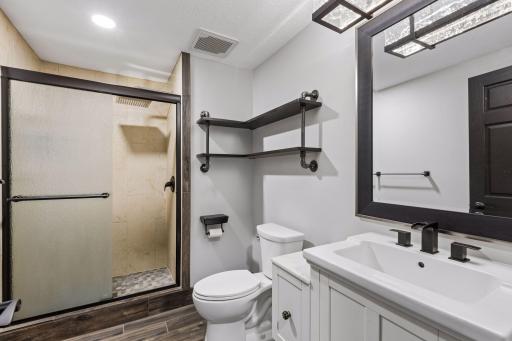 The remodeled three-quarter bathroom in the lower level features a tiled shower with rain-glass doors, modern fixtures, and convenient open shelving.