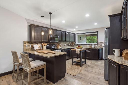 The spacious kitchen offers rich espresso-finished cabinetry, granite countertops, a tile backsplash, and generous workspace for cooking and entertaining. The breakfast bar perfectly complements this amazing kitchen.