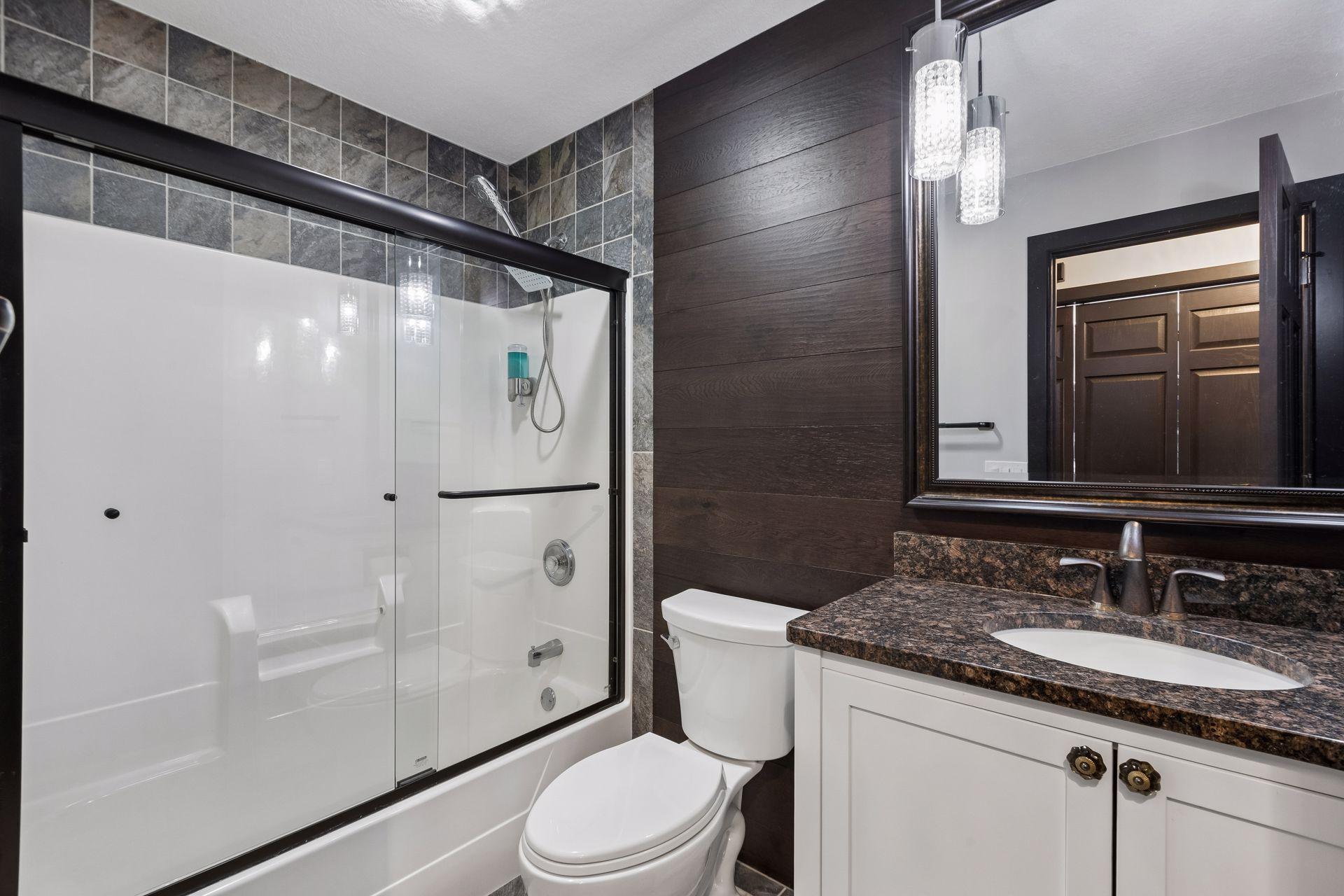 This completely remodeled main-level full bathroom features custom tile accents, a glass shower enclosure, updated fixtures, and coordinated finishes.