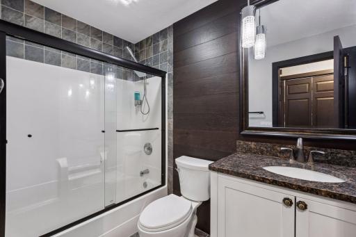 This completely remodeled main-level full bathroom features custom tile accents, a glass shower enclosure, updated fixtures, and coordinated finishes.