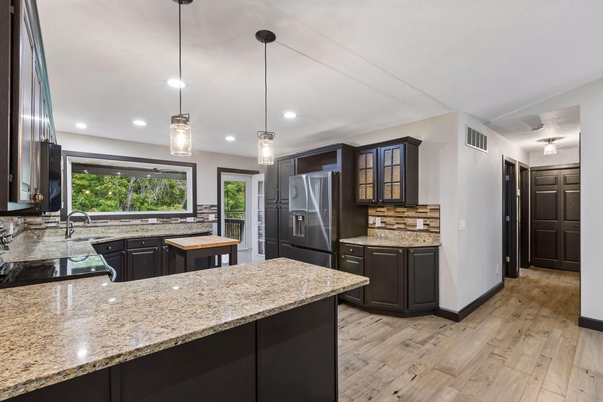 Black stainless-steel appliances, updated pendant lighting, ample cabinetry, and a pantry with pull-out drawers create a polished, functional kitchen.