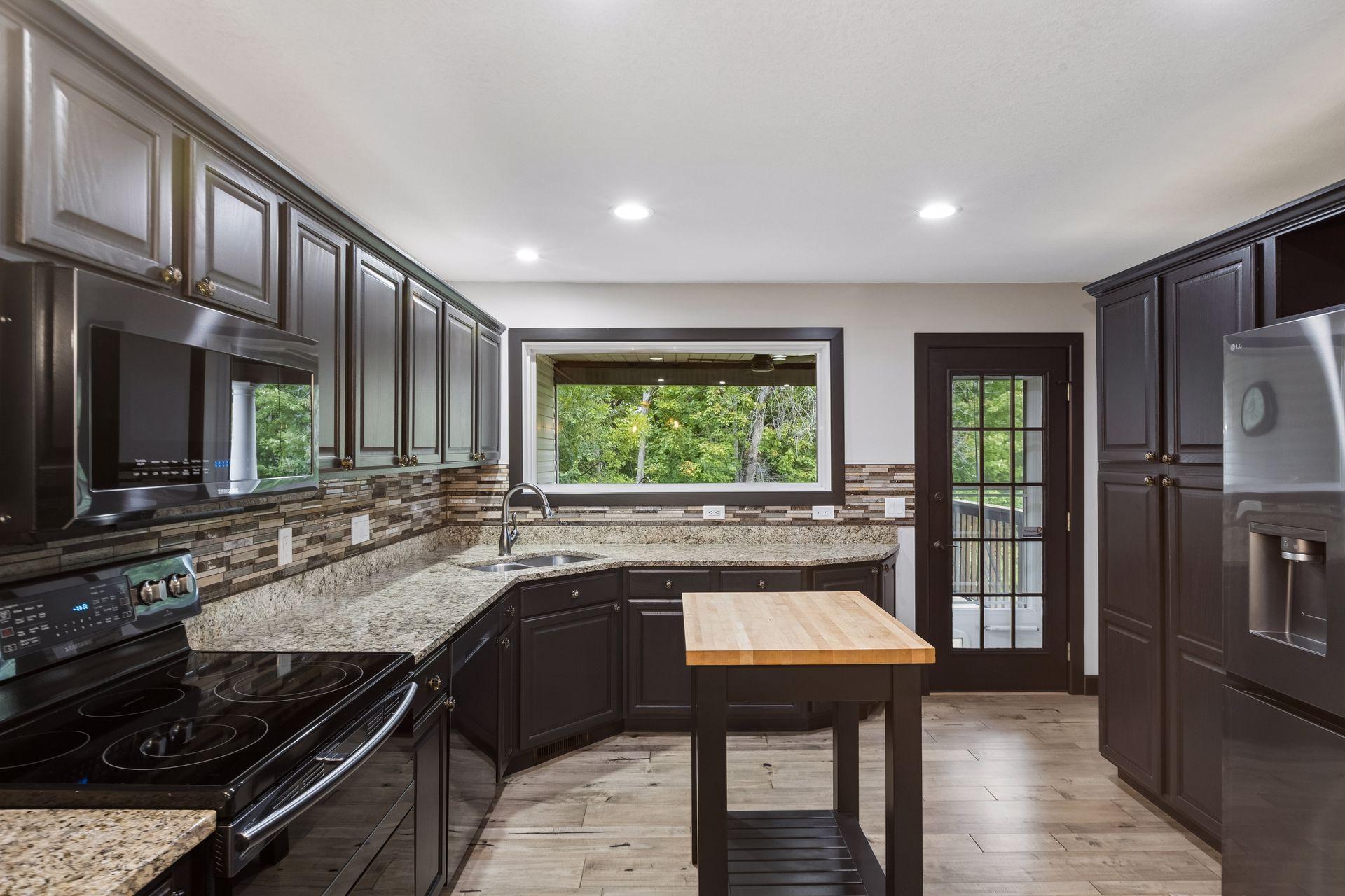 A large window above the sink frames the peaceful wooded backdrop, while the nearby door provides easy access to the covered deck.