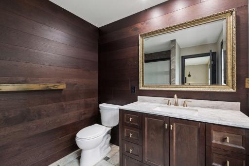 The completely remodeled primary bathroom features a furniture-style vanity with a marble top, updated fixtures, and rich wood-plank accent walls.