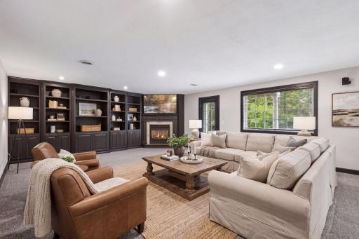 A large window and walkout access bring natural light into the family room while connecting the space to the outdoors, the covered patio, and the wooded backdrop.