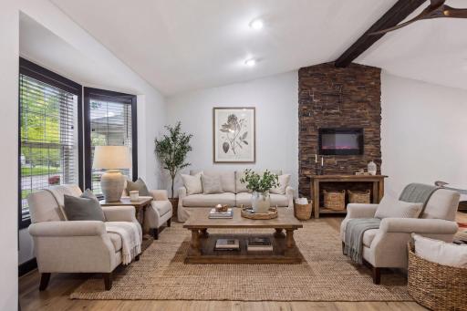 A large bay window floods the living room with natural light, and the dramatic stacked-stone fireplace creates a warm and inviting feel.