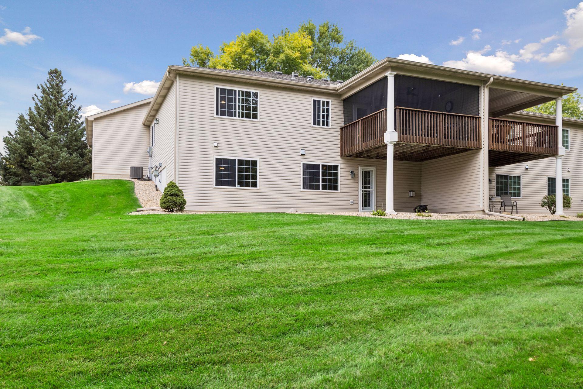 The rear view highlights the home’s walkout lower level, covered patio, screened deck, and expansive shared green space.