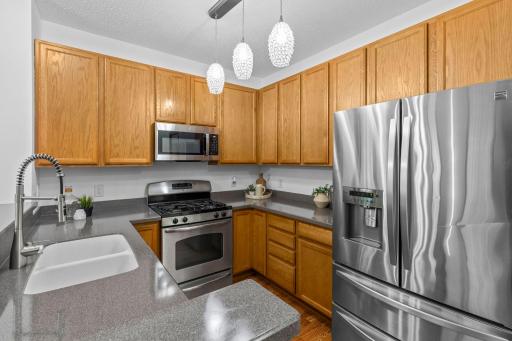 The kitchen offers ample cabinetry and counter space, breakfast bar seating, stainless steel appliances, and stylish pendant lighting.
