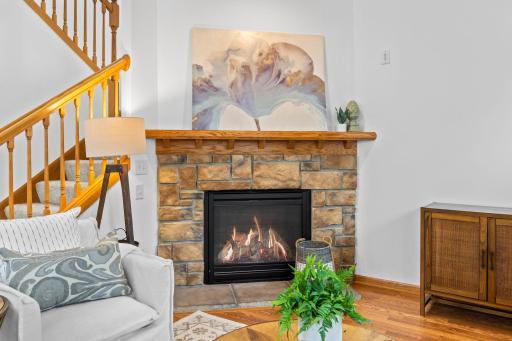 The adjacent living room is comfortable and light-filled, highlighted by a cozy gas-burning fireplace with a brick surround and wood mantel.
