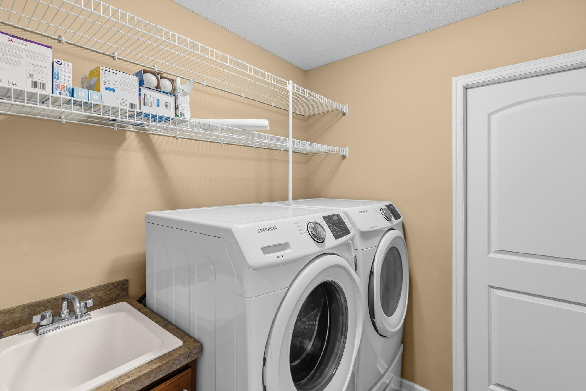 Laundry with utility sink, cuboards, shelves and utility room behind the pocket door