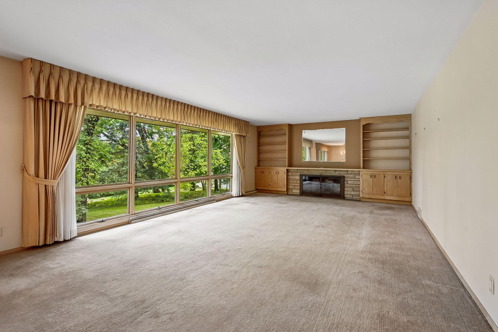 Spacious living room features a wall of windows overlooking the yard and a fireplace flanked by bookcases.
