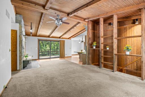 Dramatic vaulted wood ceilings with exposed beams bring warmth and character to this spacious living area, highlighted by a striking floor-to-ceiling stone fireplace. Open, custom shelving.