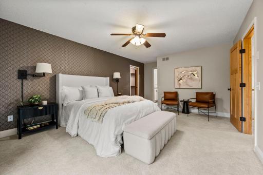 The primary suite is complete with comfortable carpeting, an accent wall, and wall sconces.