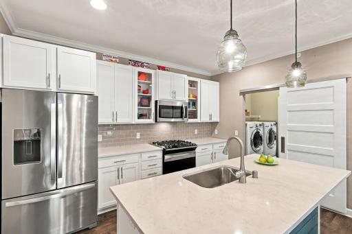 Gas range, quartz island with sink & glass pendants and accent cabinet doors