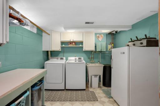 Neat and orderly laundry room offering utility sink, newer washer & dryer. Rolling table for folding/storage will stay with home.
