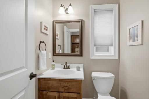 A conveniently located powder room features a warm wood vanity, bright countertop, framed mirror and a window for natural light.