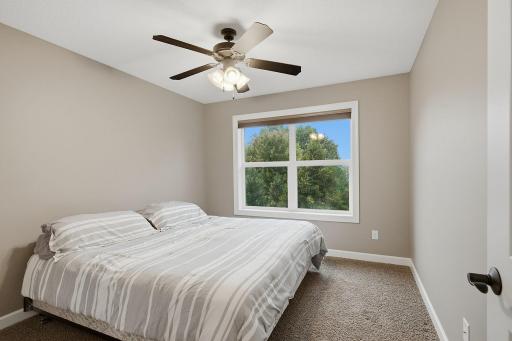 This comfortable upper-level bedroom features a large window with views of the front yard, generous natural light and a ceiling fan for added comfort.