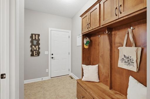 A convenient garage-entry mudroom features durable tile flooring & custom built-in cabinetry with a bench, coat hooks & upper cabinets, creating a designated drop zone with for everyday essentials. A closet is also available for your storage needs.