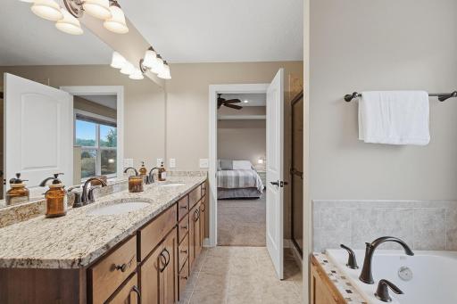The private ensuite features a long granite-topped vanity with dual sinks, abundant cabinetry and an expansive wall mirror. The layout separates the vanity area from the soaking tub and step-in shower for added functionality.