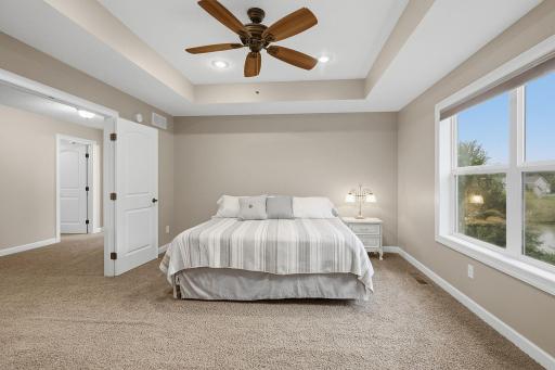 The spacious primary bedroom features a striking box-vault ceiling with recessed lighting and a ceiling fan. An oversized window adds natural light while offering a peaceful view of the backyard.