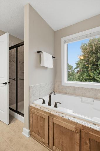 A generous soaking tub creates a relaxing retreat, surrounded by tile detailing and positioned beneath a large window for abundant natural light. The separate step-in shower is conveniently located alongside the tub.