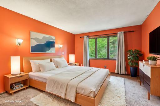 Supportive primary suite with windows onto greenery, virtually staged