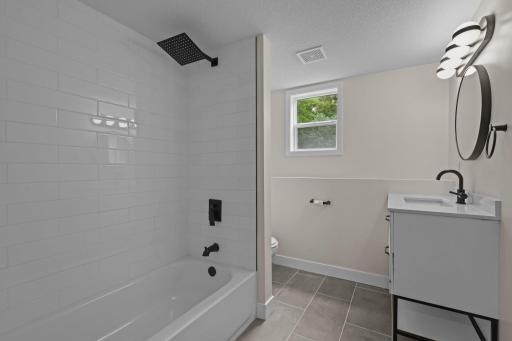 Newly remodeled lower level bath, complete with tub, tile surround, tile floors, new vanity and toilet.