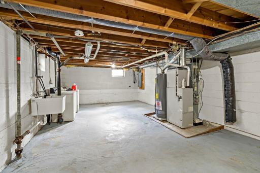 Unfinished lower level utility area with washer/dryer and laundry sink.