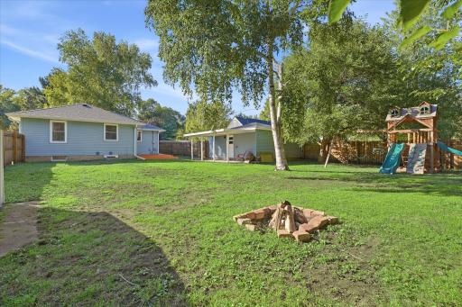 Mature trees, a firepit, playset, deck, covered patio, and plenty of open lawn make this backyard a standout extension of the home.