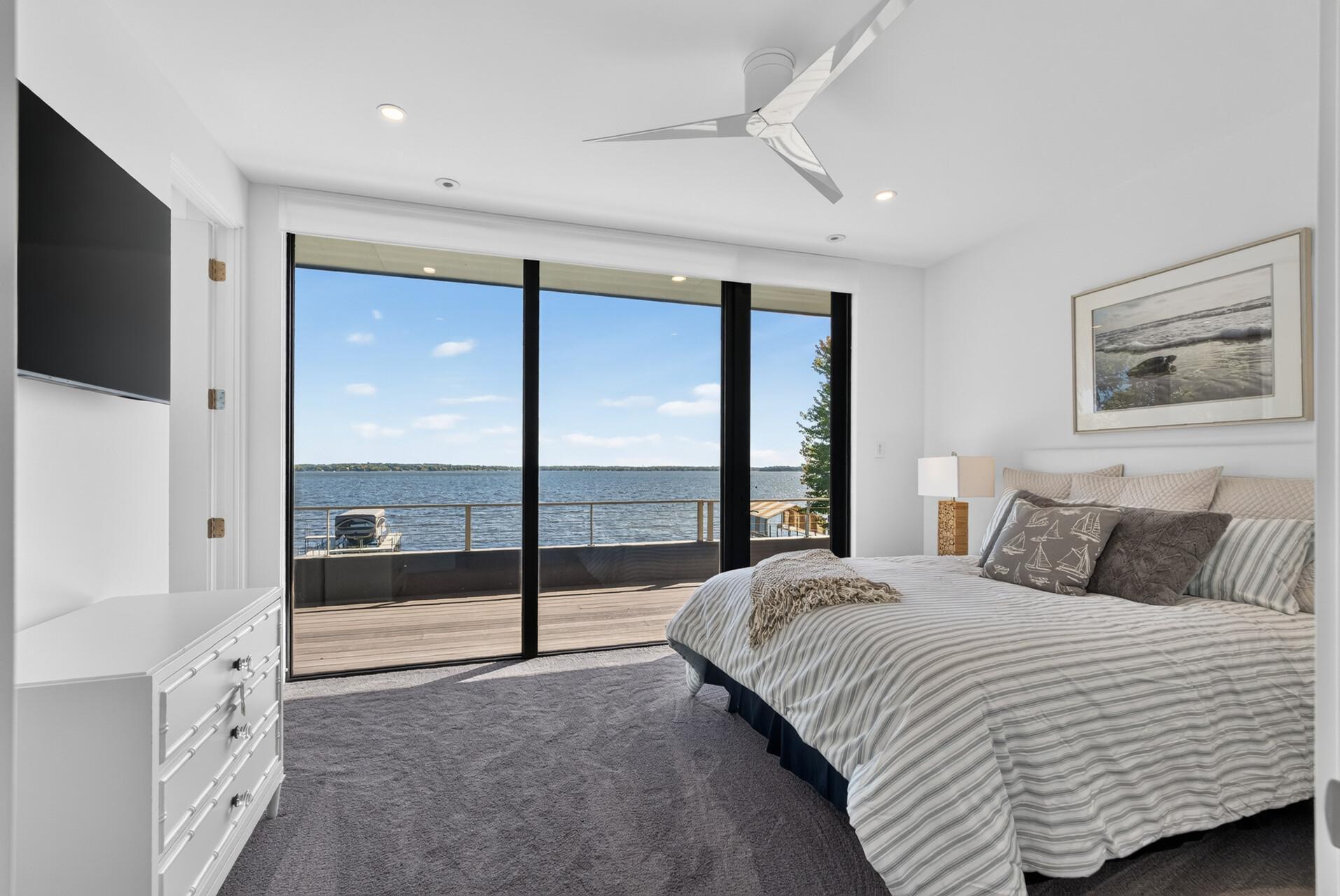Three additional upper-level bedrooms are designed alike, each with modern ceiling fans, comfortable carpeting, and south-facing windows showcasing uninterrupted lake views. (Upper-level bedroom #2)
