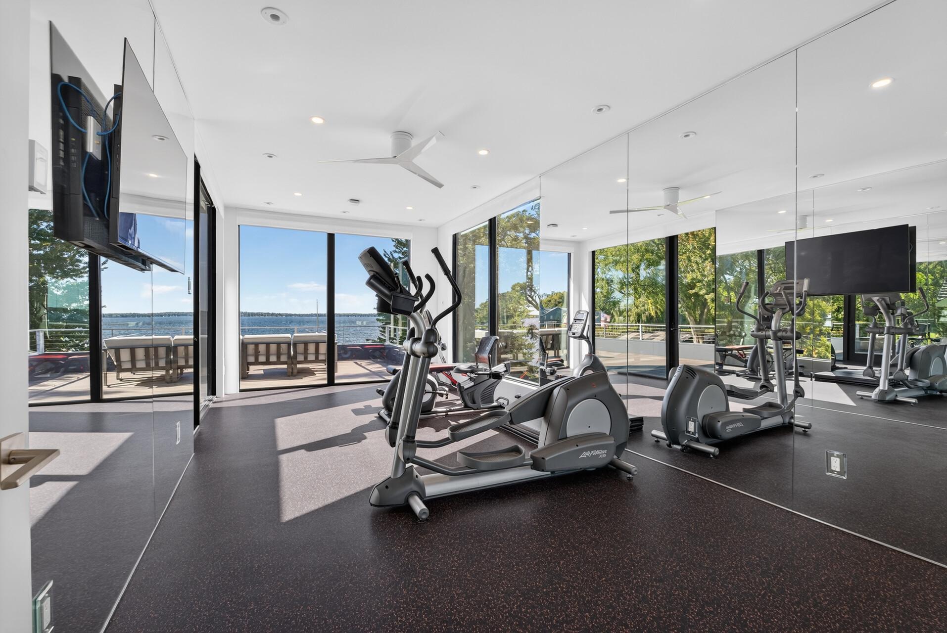 A dedicated fitness room features fitness flooring and floor-to-ceiling mirrors spanning several walls.