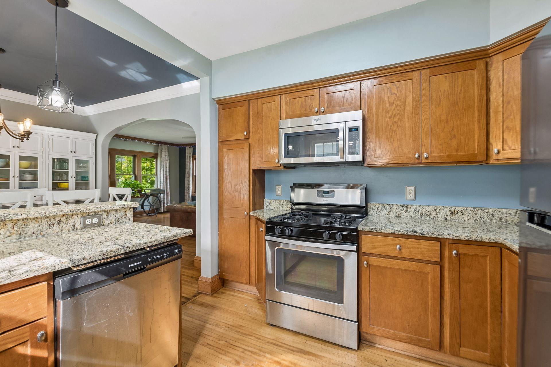 A gas range, a built-in microwave, and a tall pantry cabinet give you room to cook and store. The arched doorway beyond keeps you connected to the rest of the main level.