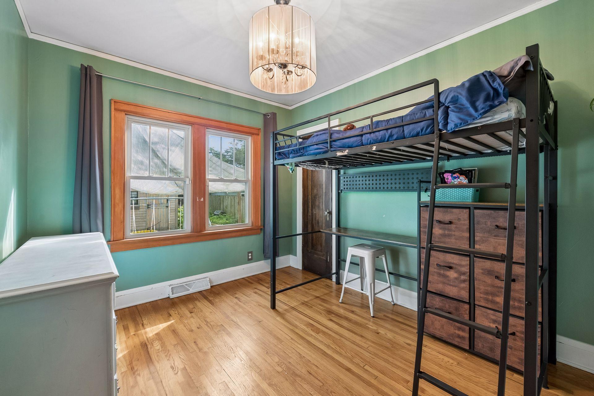 This main level bedroom has hardwood floors, warm wood window trim, and a statement light fixture. Large windows look out over the backyard.