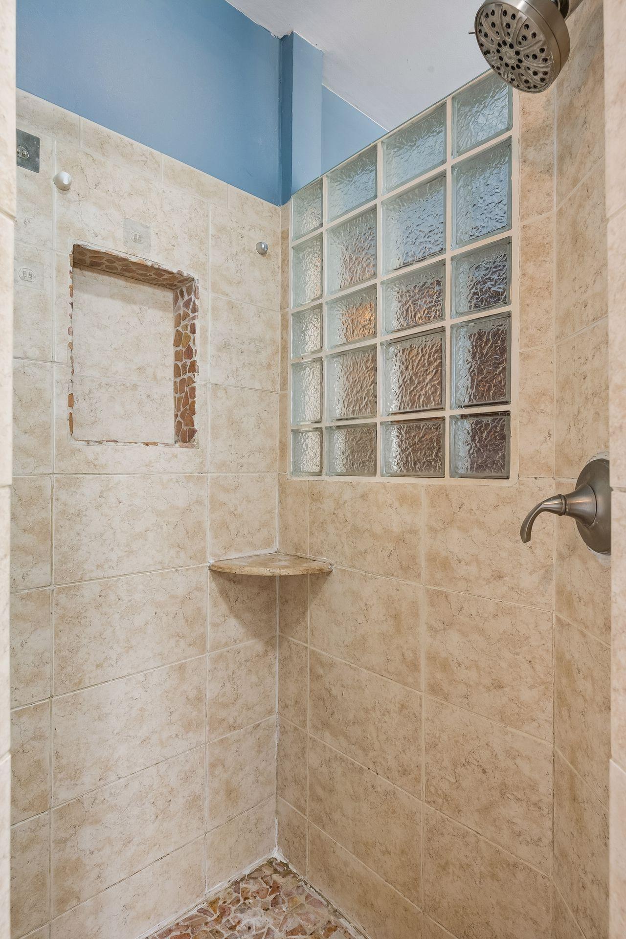 A separate tiled shower with a recessed niche, a corner shelf, and a glass block window rounds out this spacious bath.