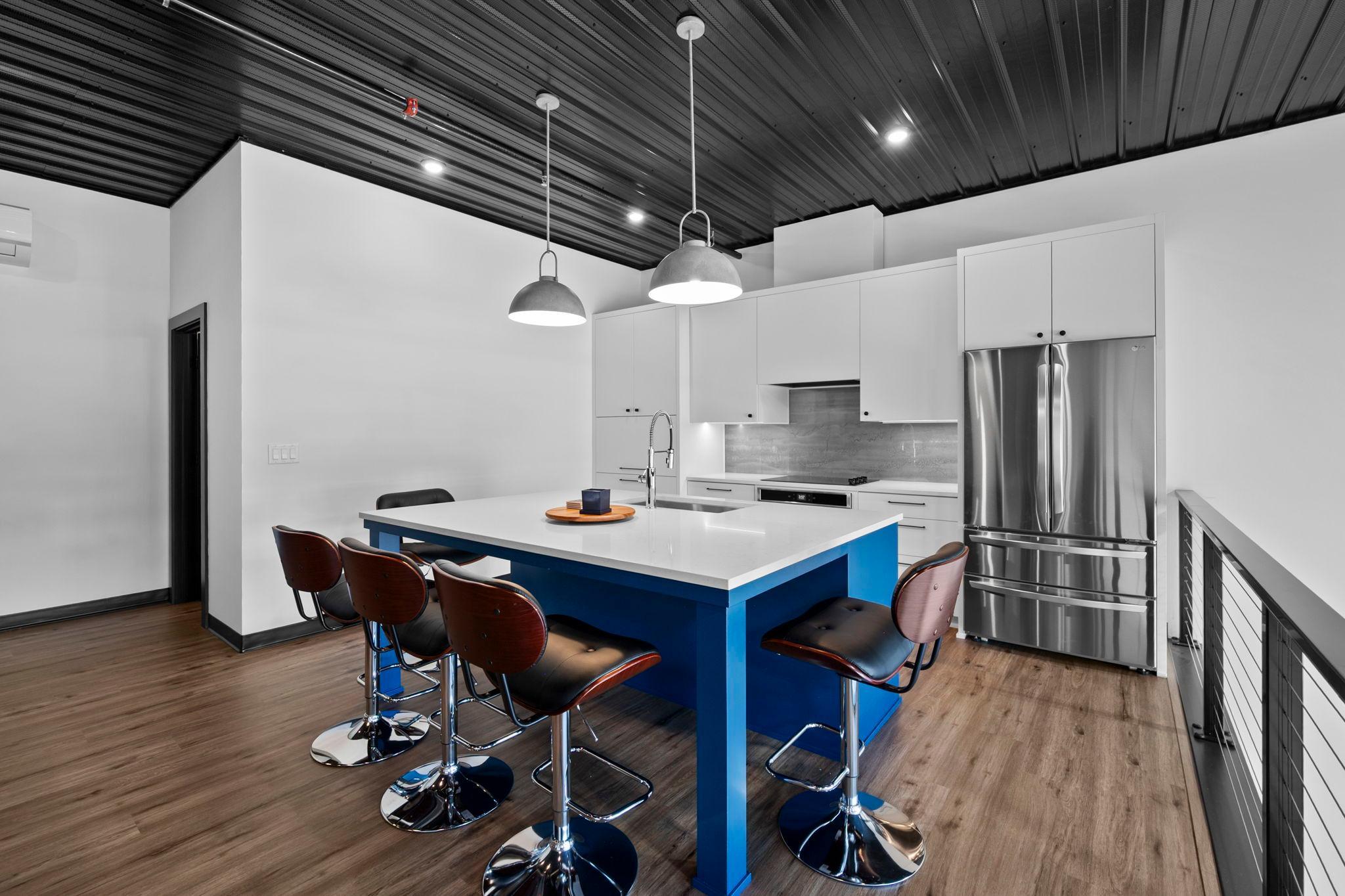 The full kitchen offers custom cabinetry, center island with breakfast bar seating, LG refrigerator, cooktop, oven, microwave, dishwasher, and a unique glass-cover backsplash.