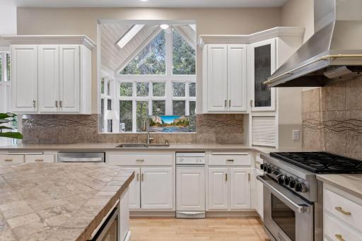 Kitchen sink is positioned beneath dramatic vaulted windows, filling the space with natural light and wooded backyard views.