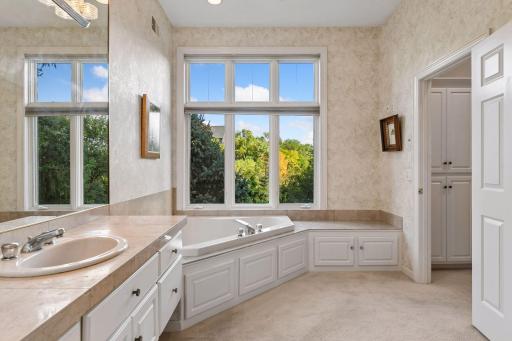 Spa-like primary bath features a large soaking tub positioned beneath a picture window overlooking the trees.