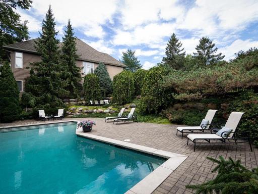 Beautifully landscaped backyard offers multiple outdoor gathering spaces surrounded by mature trees and natural stone.