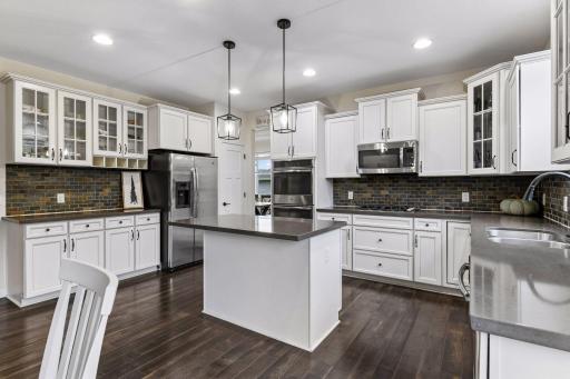 Chefâs kitchen designed for gathering and entertaining, featuring double wall ovens, center island, cabinetry with glass-front accents, stainless steel appliances, and stylish finishes. Open layout flows seamlessly into the dining and living spaces.