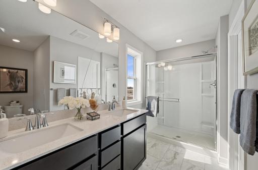 (Photo of model home, actual features may vary) Dual quartz sinks with a full wall-width vanity mirror and a luxe glass-enclosed shower creates a spa-like atmosphere in the en-suite bathroom