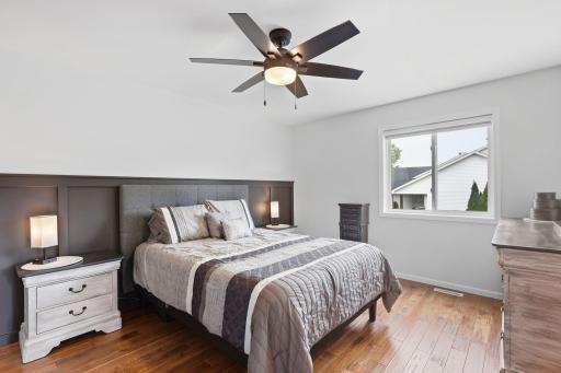 Primary bedroom with beautiful hickory flooring, decorative wood paneled wall, updated lighting with ceiling fan.